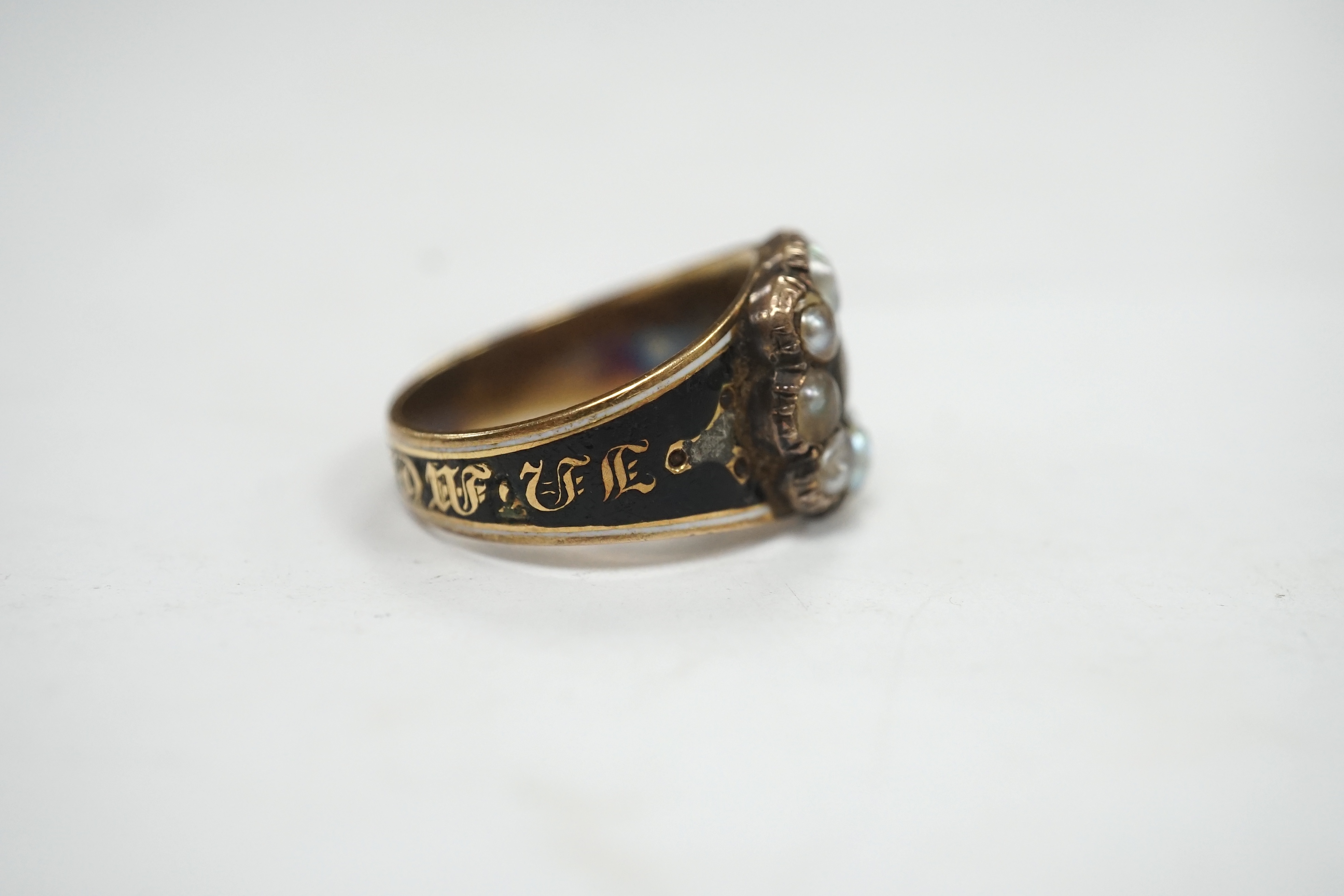 A late George III yellow metal, two colour enamel and split pearl set mourning ring, with plaited hair beneath a glazed panel, inscribed, 'M.J. Escott died 12th July, 1817 aged 21', size N, gross weight 6.8 grams. Condit